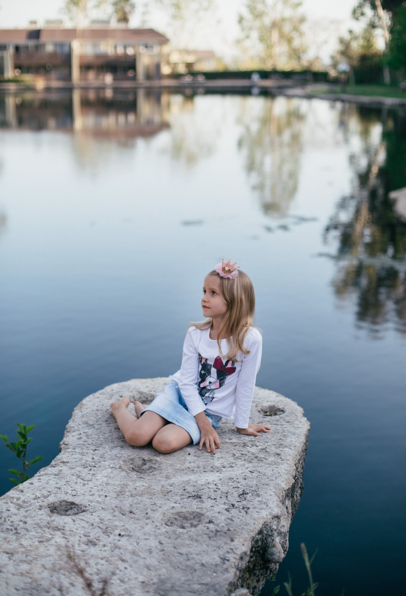 toddler girl sitting on gray stone beside body of water at daytime
